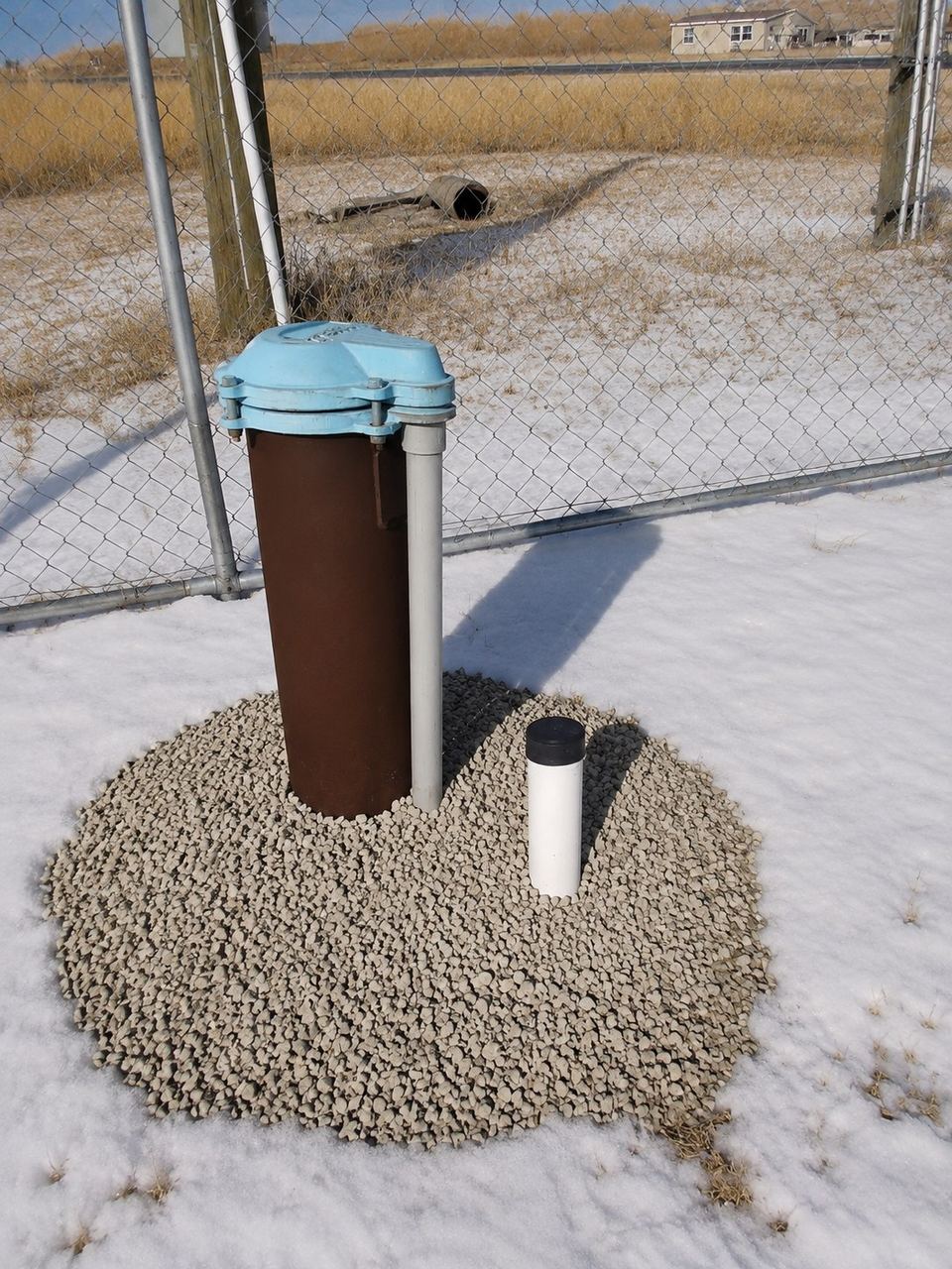 Water well head casing with a sanitary cap on a gravel well pad